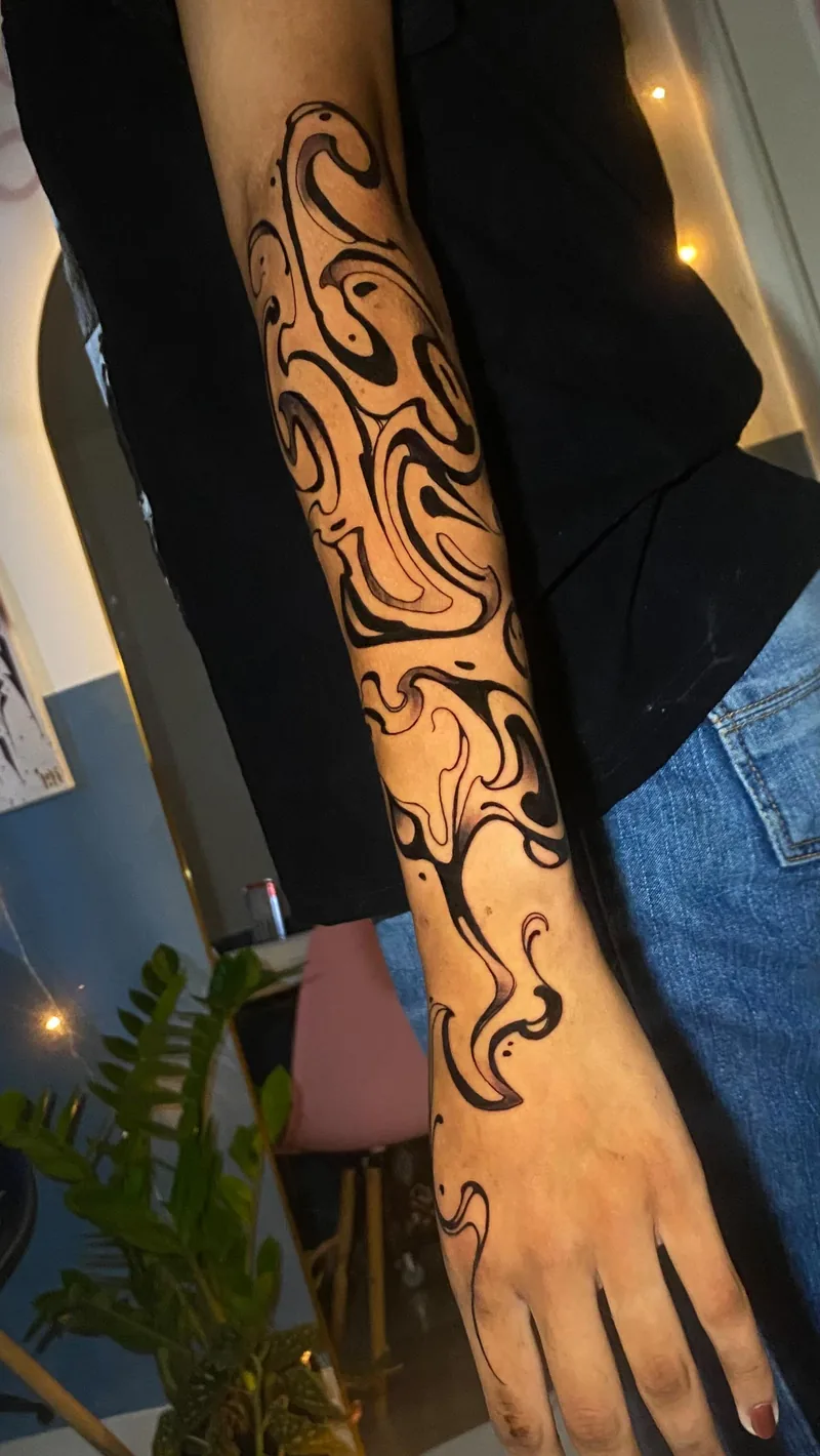 Tatuagem de desenho fluido em tinta preta, com curvas e formas abstratas que percorrem o braço até o dorso da mão